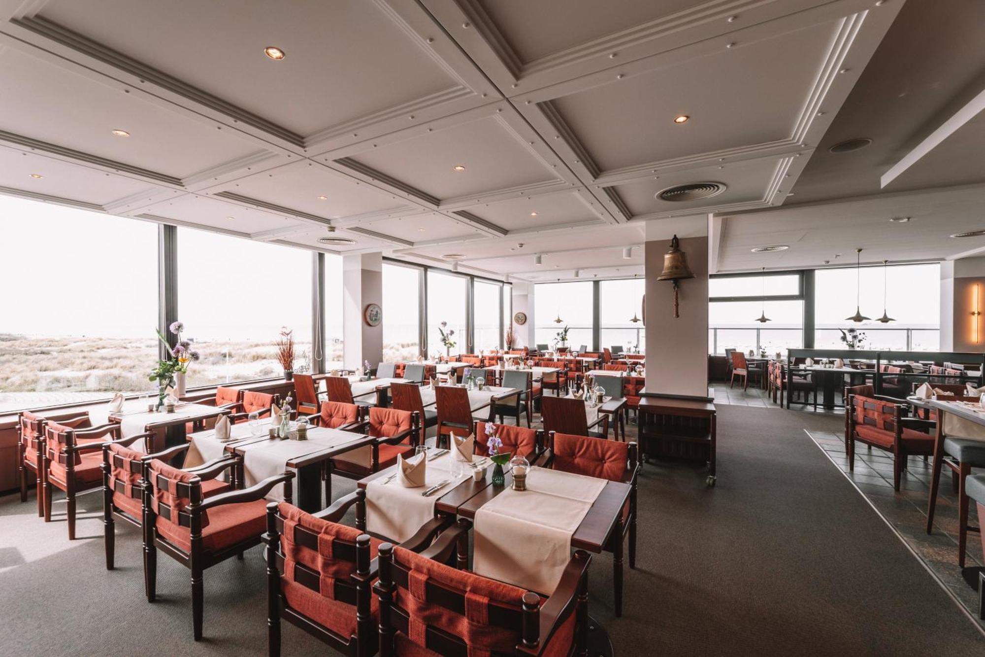 Hotel Neptun Rostock Exterior photo The photo shows the interior of a restaurant. It features several tables, each set with tablecloths and flowers, creating a welcoming atmosphere. The furniture includes red and wooden chairs, contributing to a comfortable dining environment. Large wi