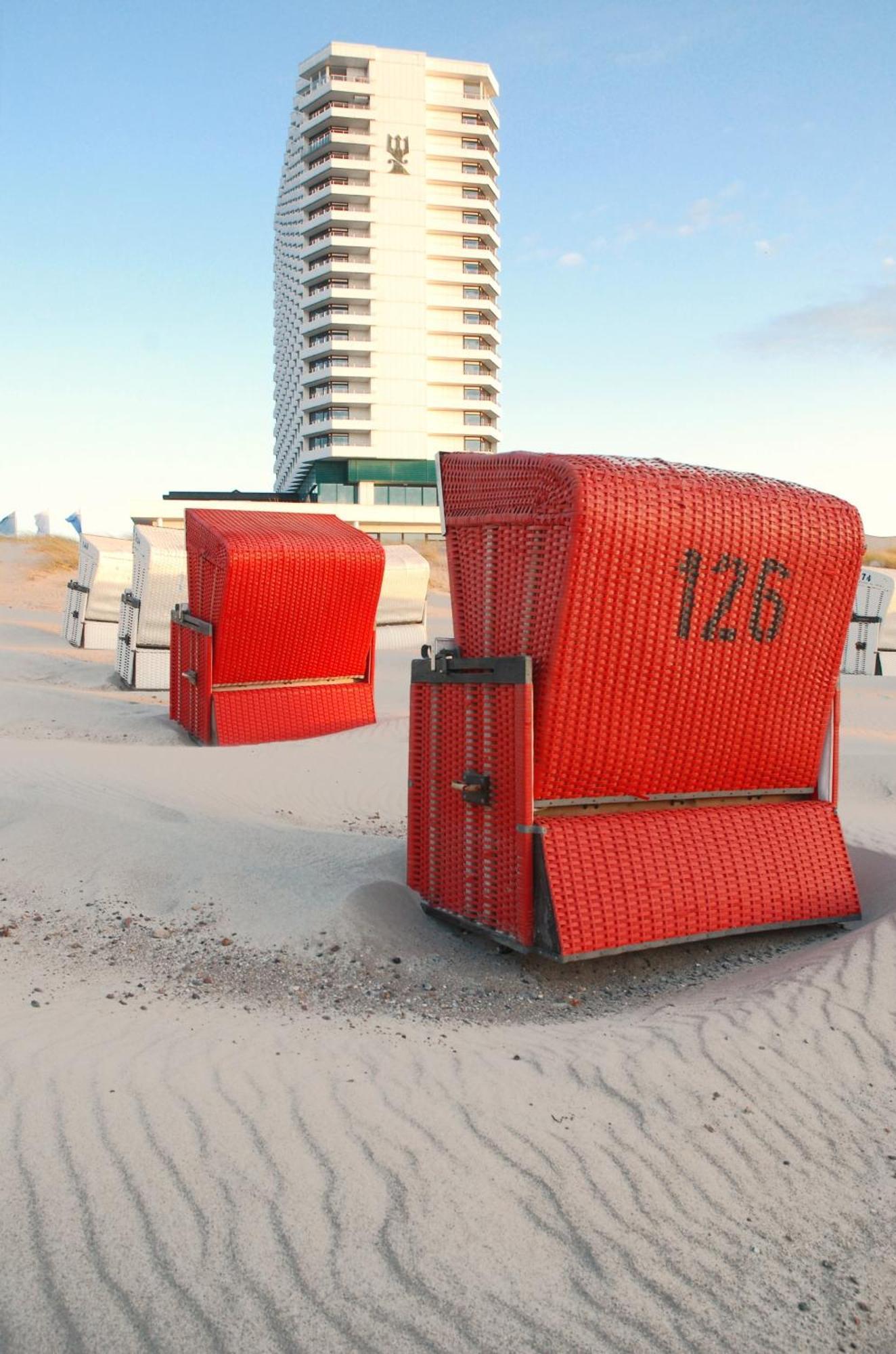 Hotel Neptun Rostock Exterior photo The photo shows several brightly colored beach chairs or cabanas in a sandy area, likely near a beach. The chairs are a vivid red color and are arranged in a way that suggests they are set up for visitors. One of the chairs has the number "126" promi