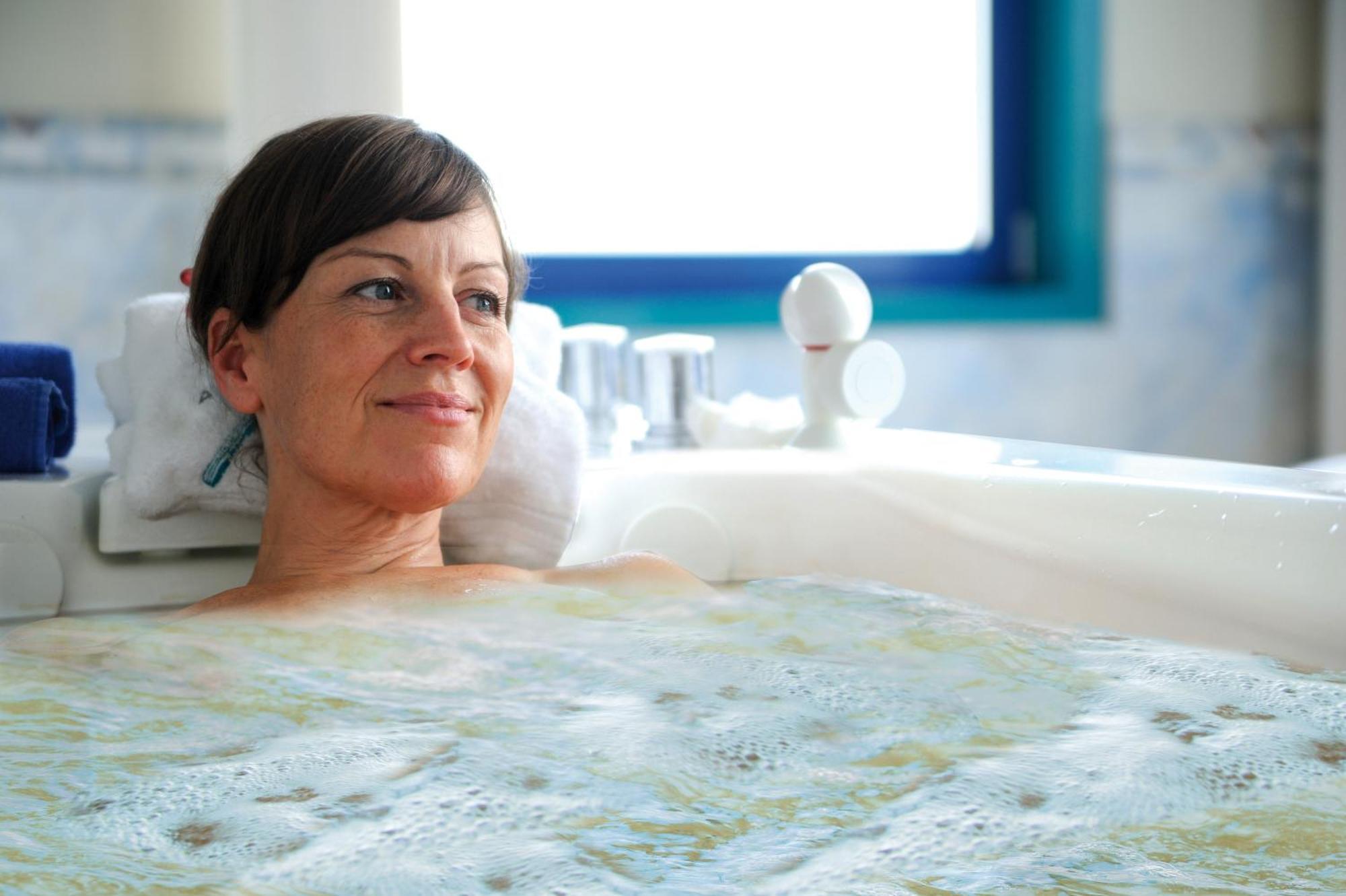 Hotel Neptun Rostock Exterior photo The photo shows a woman relaxing in a bathtub filled with water. She has a calm expression on her face and is partially submerged, with bubbles visible around her. The setting appears to be bright and modern, with a window in the background allowing 