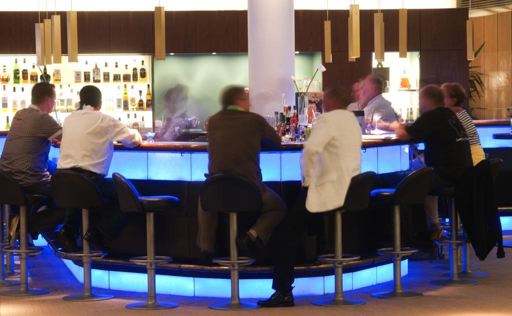 Hotel Neptun Rostock Exterior photo The photo depicts a modern bar scene with several people seated at a circular bar. The bar features a glowing blue light underneath, creating a vibrant atmosphere. In the background, bottles of various alcoholic beverages are visible on shelves, indi