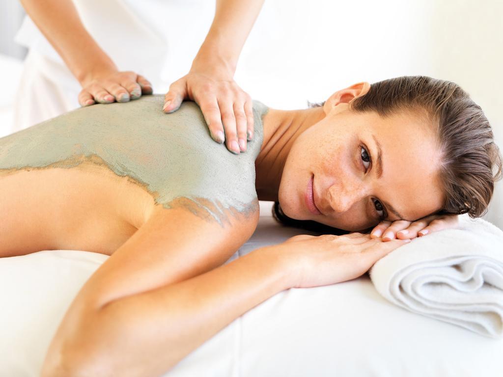 Hotel Neptun Rostock Exterior photo The photo shows a woman lying on a massage table receiving a treatment. A person is applying a green mud or clay substance to the woman's back. The environment appears calm and relaxing, with soft lighting and a clean, spa-like setting. The woman loo