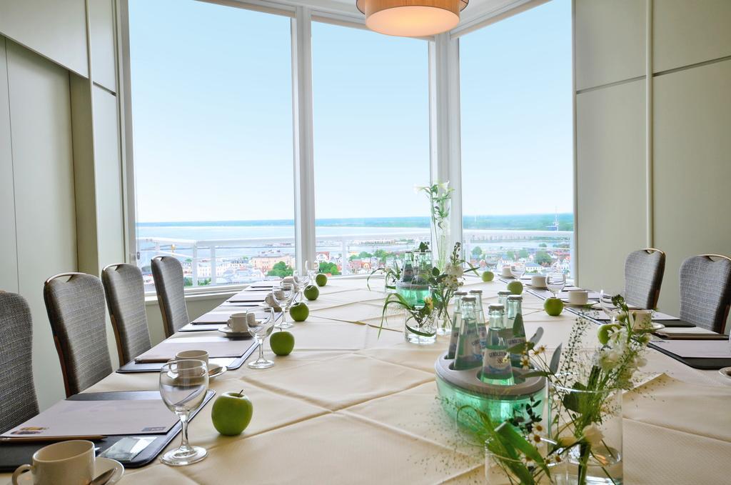 Hotel Neptun Rostock Exterior photo The photo shows a modern conference room with large windows that provide a view of the outside, possibly overlooking a body of water or a cityscape. The table is elegantly set with a neutral tablecloth and features several elements that enhance the d