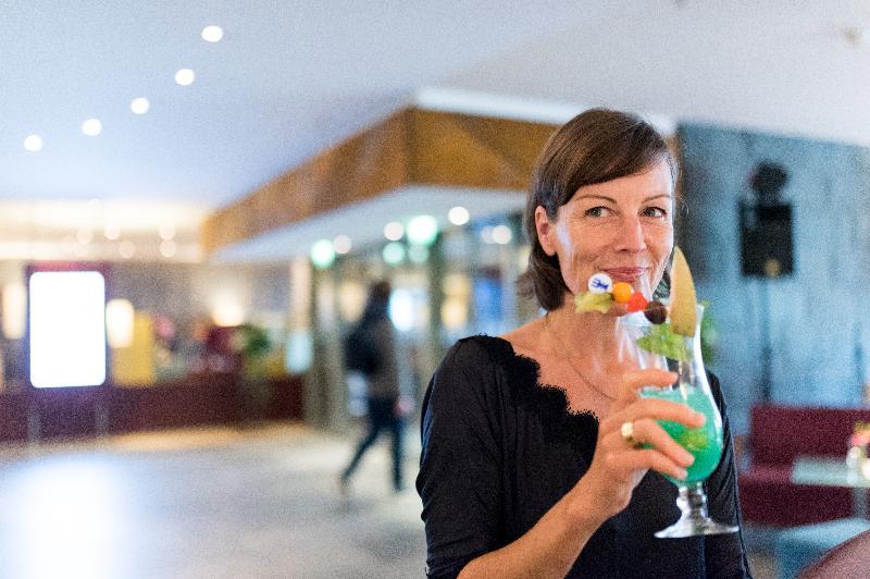 Hotel Neptun Rostock Exterior photo The photo shows a woman holding a colorful tropical drink in a stylish glass. The drink is bright green and garnished with fruits and colorful decorations like a small umbrella and a straw. The setting appears to be an upscale venue, with soft lighti