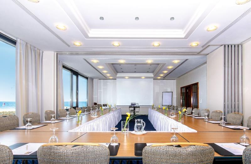 Hotel Neptun Rostock Exterior photo The photo shows a modern conference room set up for a meeting or event. The room features a large table arranged in a U-shape, surrounded by elegant chairs. There are glasses and water pitchers on the table, along with small flower arrangements for d