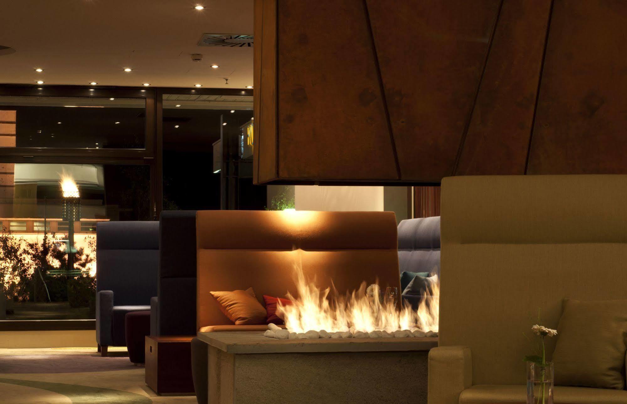 Hotel Neptun Rostock Exterior photo The photo depicts a stylish and modern interior space, likely within a lounge or hotel lobby. In the foreground, there is a cozy seating area with comfortable couches and cushions in neutral tones. A striking feature is a contemporary fireplace that 