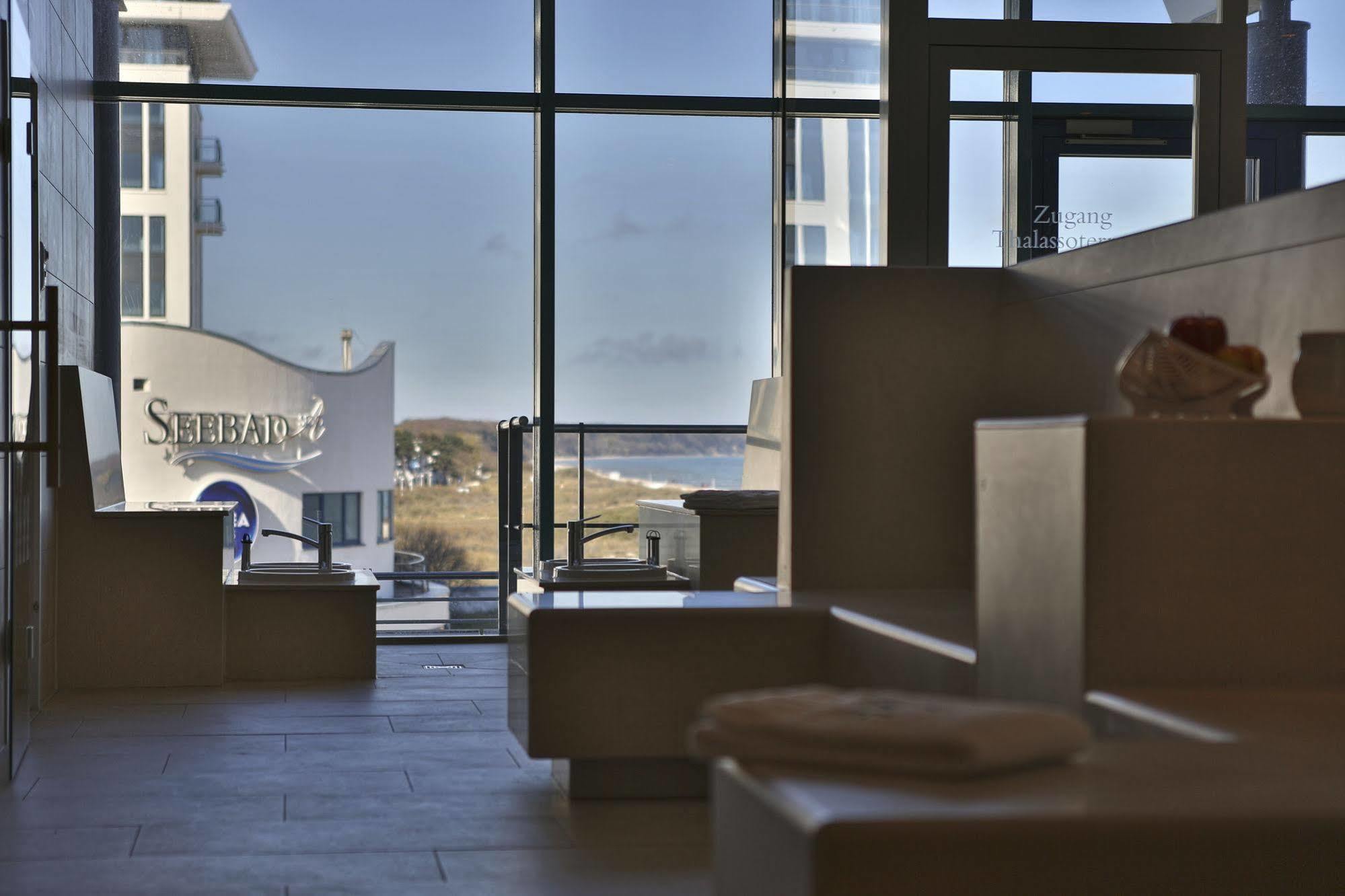 Hotel Neptun Rostock Exterior photo The photo shows a modern interior space with large windows allowing natural light to flood in. There are sleek, minimalist seating areas or steps made of a light-colored material. In the background, through the glass, you can see a sign for "Seabed,"