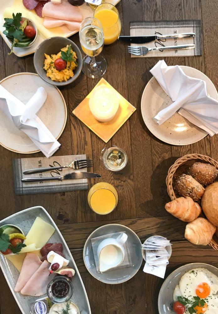 Hotel Neptun Rostock Exterior photo The photo displays a dining setup featuring a wooden table with various food items. There are two plates set at the table, alongside white napkins elegantly folded. A small square plate with a lit candle sits in the center. To one side, there's a gla