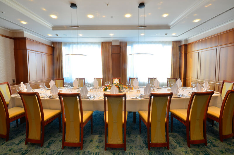 Hotel Neptun Rostock Exterior photo The photo shows a beautifully arranged dining room. There is a long rectangular table set for a formal meal, with white tablecloths and neatly arranged place settings that include plates, cutlery, and folded napkins. The chairs around the table have 