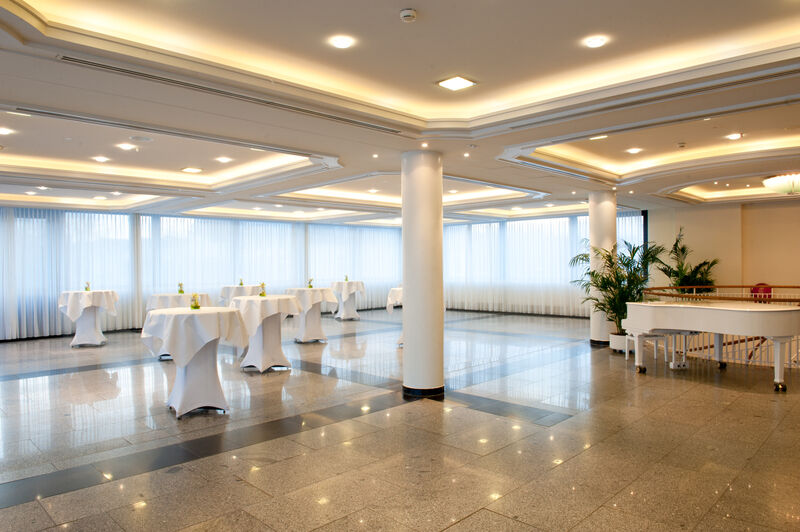 Hotel Neptun Rostock Exterior photo The photo shows a spacious, well-lit event room. The ceiling features modern lighting, and large windows allow natural light to fill the space. There are several round tables draped in white tablecloths, placed throughout the room. The flooring appea